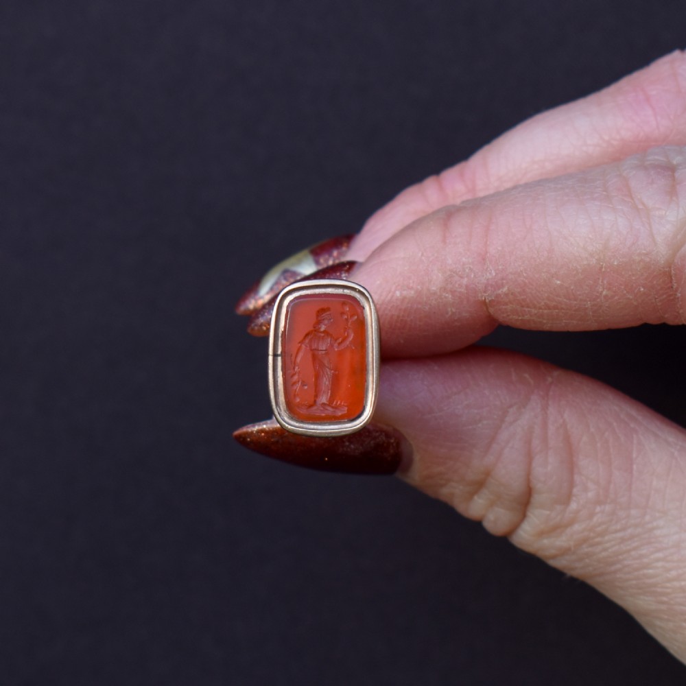 An antique gold fob pendant set with a rectangular orange carnelian gemstone carved with a classical standing figure holding a branch. View II