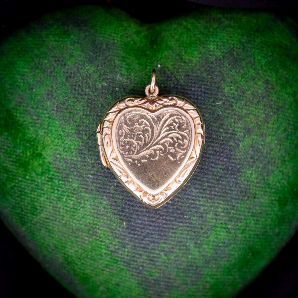 A vintage 9ct yellow gold heart-shaped locket pendant featuring engraved botanical scrollwork and a decorative scrolled border.
