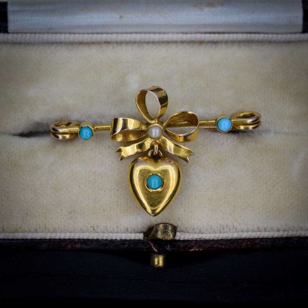 An antique yellow gold bar brooch featuring a central bow motif with a seed pearl, a dangling gold heart set with a turquoise cabochon, and two flanking turquoise stones. View IV