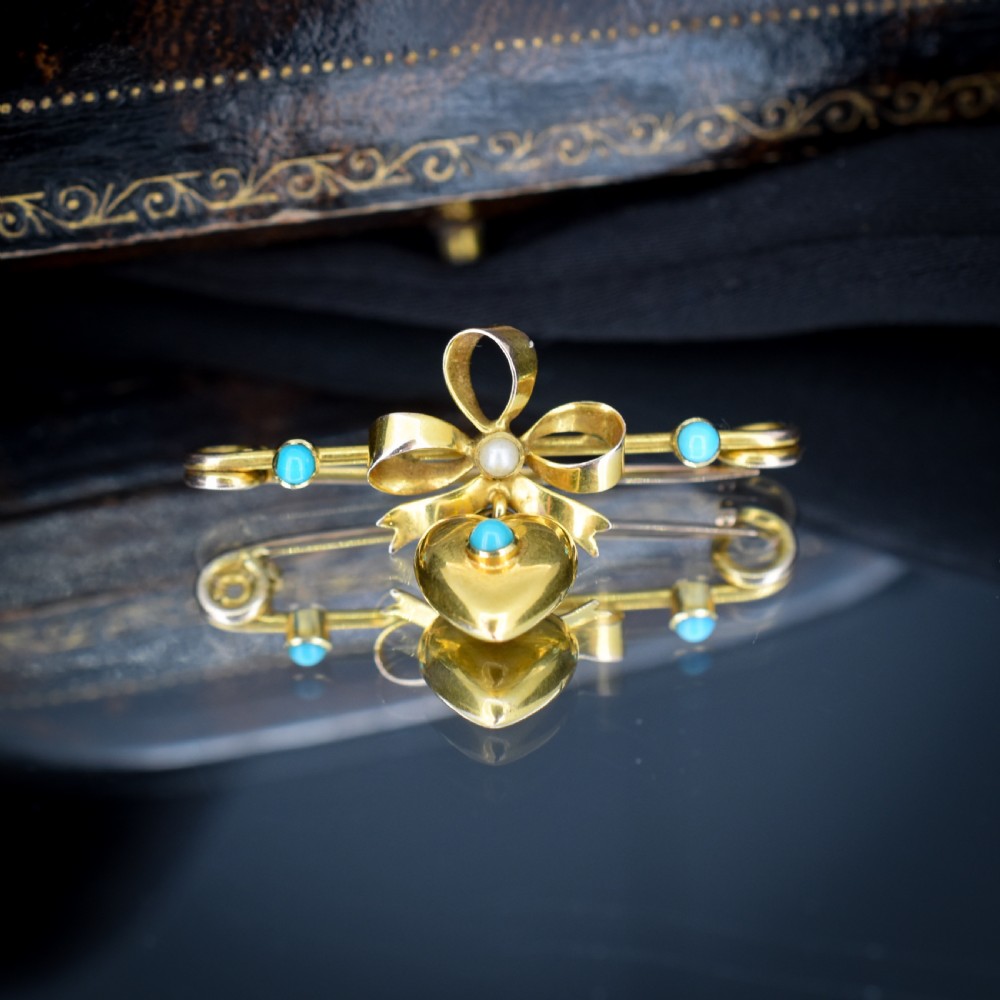 An antique yellow gold bar brooch featuring a central bow motif with a seed pearl, a dangling gold heart set with a turquoise cabochon, and two flanking turquoise stones. View V