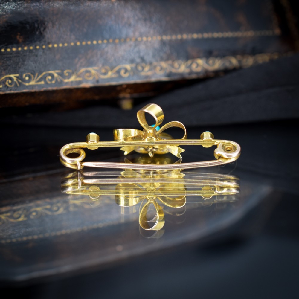 An antique yellow gold bar brooch featuring a central bow motif with a seed pearl, a dangling gold heart set with a turquoise cabochon, and two flanking turquoise stones. View VI