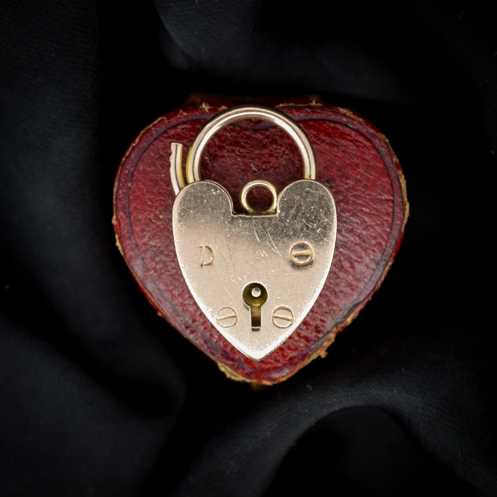 A 9ct rose gold heart-shaped padlock pendant featuring a hinged top shackle, central keyhole detail, and screw motif engravings.