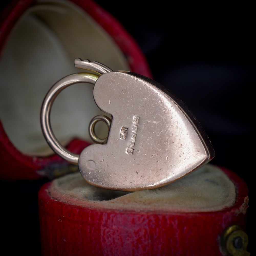 A 9ct rose gold heart-shaped padlock pendant featuring a hinged top shackle, central keyhole detail, and screw motif engravings. View VI