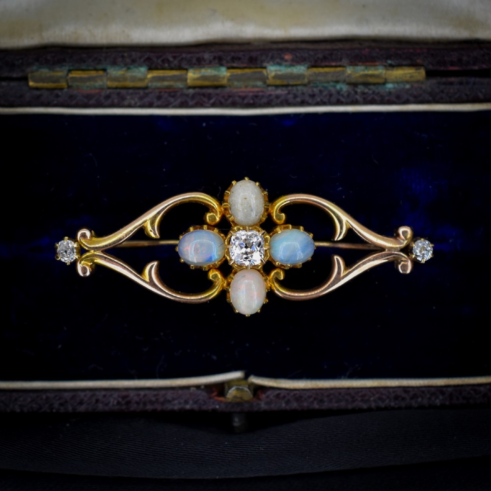 An antique 15ct gold brooch featuring four cabochon opals and central diamond accents set in an openwork scroll framing, contained inside a navy velvet presentation box. View IV