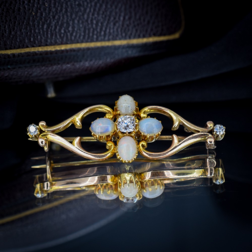 An antique 15ct gold brooch featuring four cabochon opals and central diamond accents set in an openwork scroll framing, contained inside a navy velvet presentation box. View VI