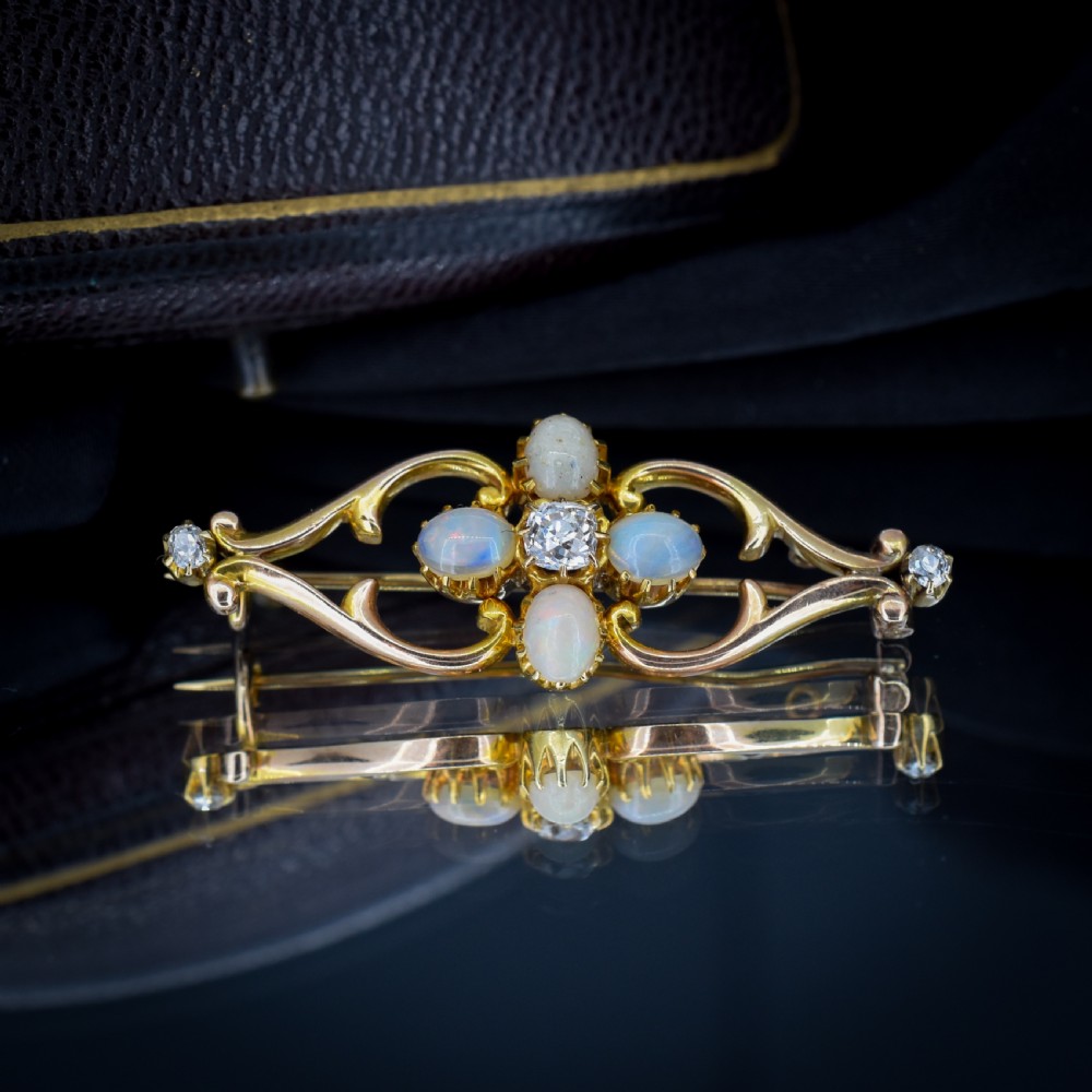 An antique 15ct gold brooch featuring four cabochon opals and central diamond accents set in an openwork scroll framing, contained inside a navy velvet presentation box. View VII