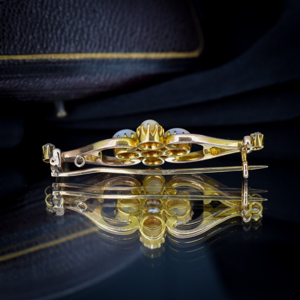 An antique 15ct gold brooch featuring four cabochon opals and central diamond accents set in an openwork scroll framing, contained inside a navy velvet presentation box. View IX