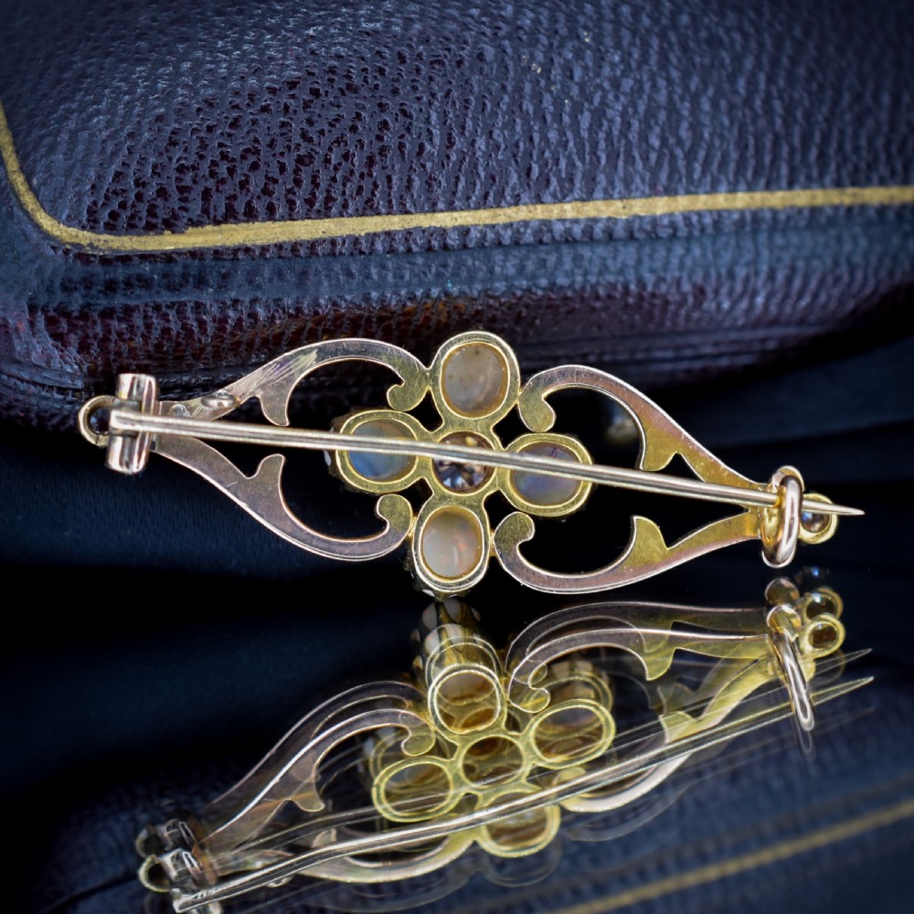 An antique 15ct gold brooch featuring four cabochon opals and central diamond accents set in an openwork scroll framing, contained inside a navy velvet presentation box. View X