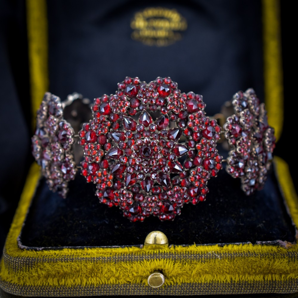An antique Victorian Bohemian garnet bracelet featuring a central starburst cluster of rose-cut deep red garnets mounted on a wide hinged band.