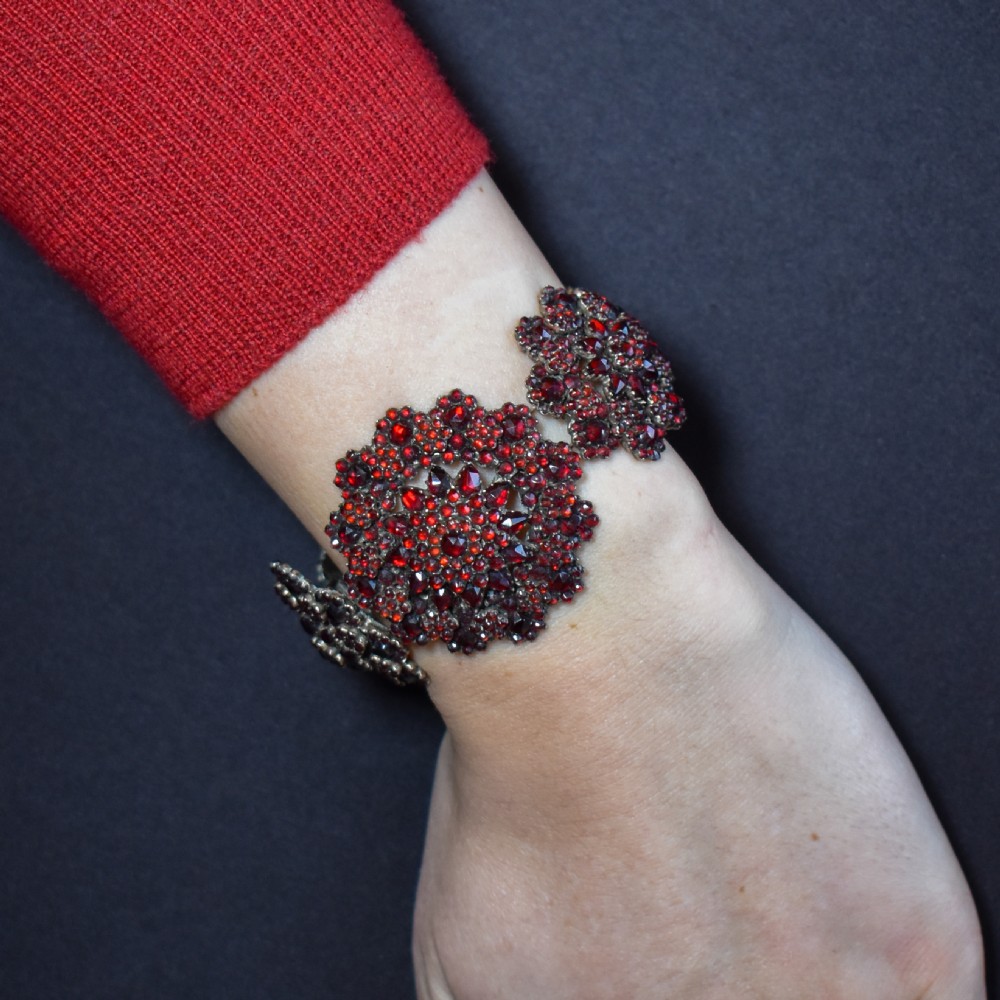 An antique Victorian Bohemian garnet bracelet featuring a central starburst cluster of rose-cut deep red garnets mounted on a wide hinged band. View V