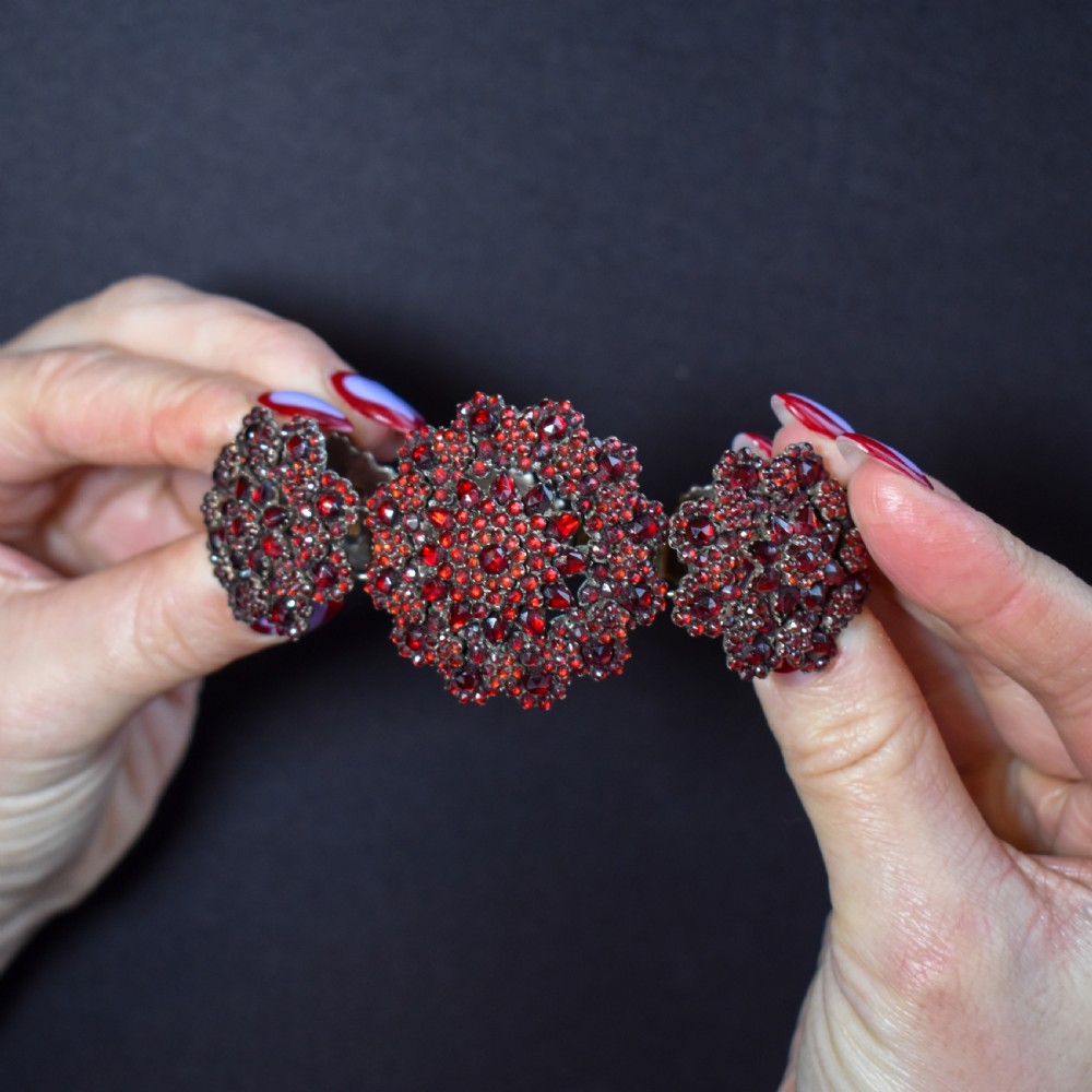 An antique Victorian Bohemian garnet bracelet featuring a central starburst cluster of rose-cut deep red garnets mounted on a wide hinged band. View VI