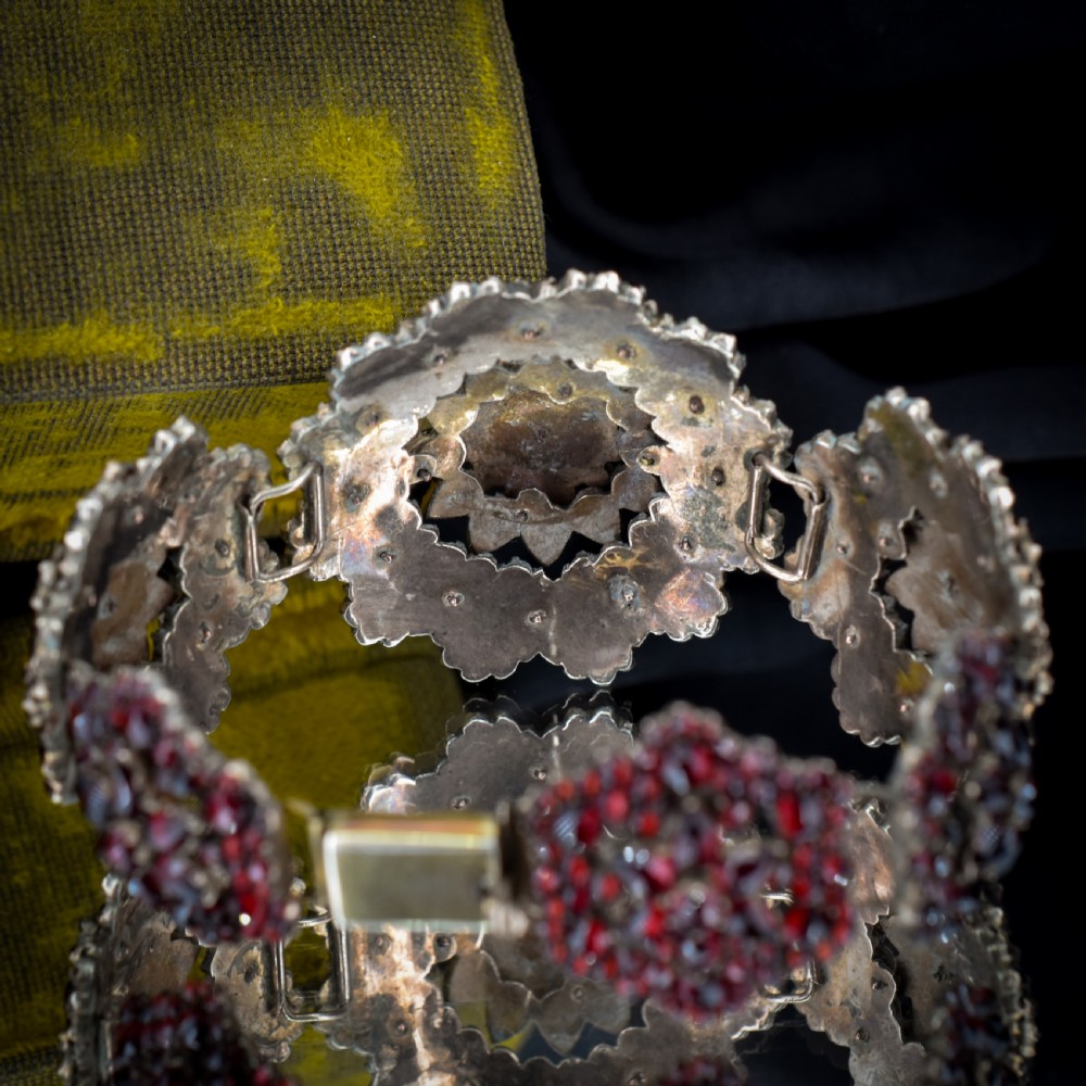 An antique Victorian Bohemian garnet bracelet featuring a central starburst cluster of rose-cut deep red garnets mounted on a wide hinged band. View IX