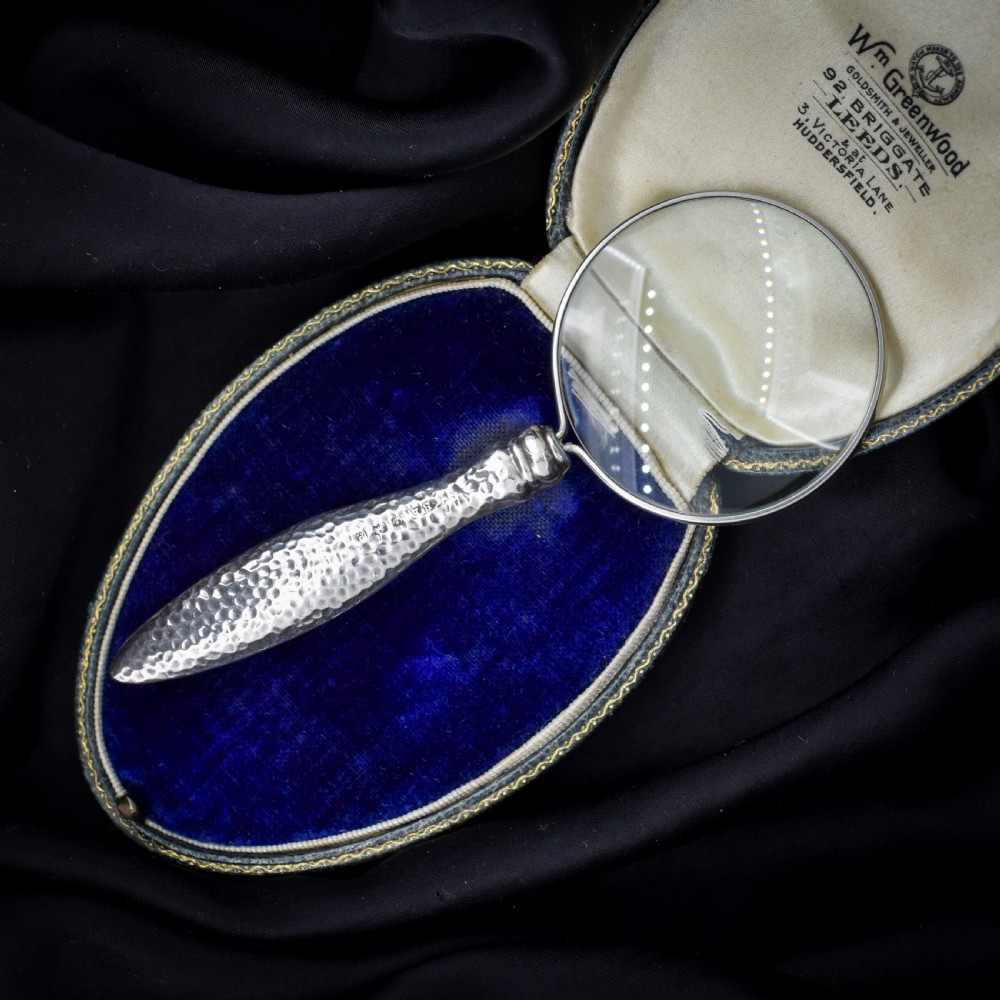 An Edwardian sterling silver magnifying glass featuring a hammered planished handle and a circular glass lens, presented inside an open velvet-lined case.