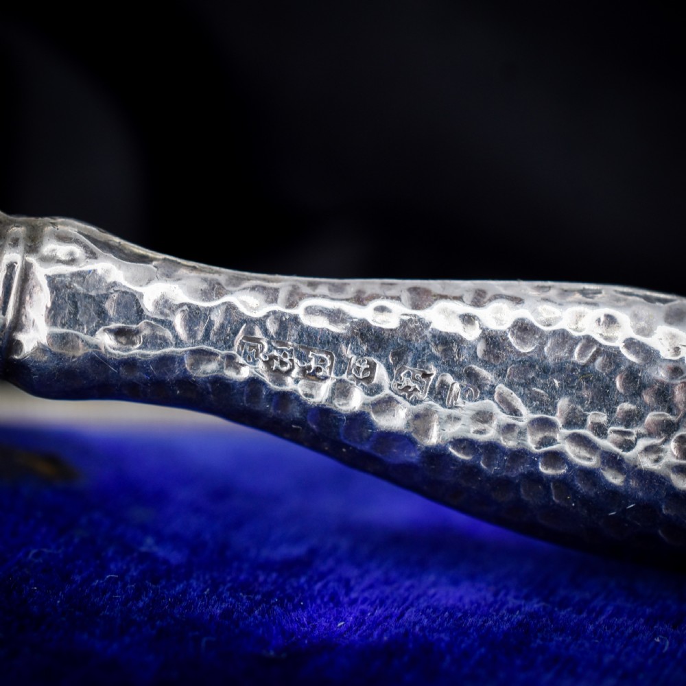 An Edwardian sterling silver magnifying glass featuring a hammered planished handle and a circular glass lens, presented inside an open velvet-lined case. View III