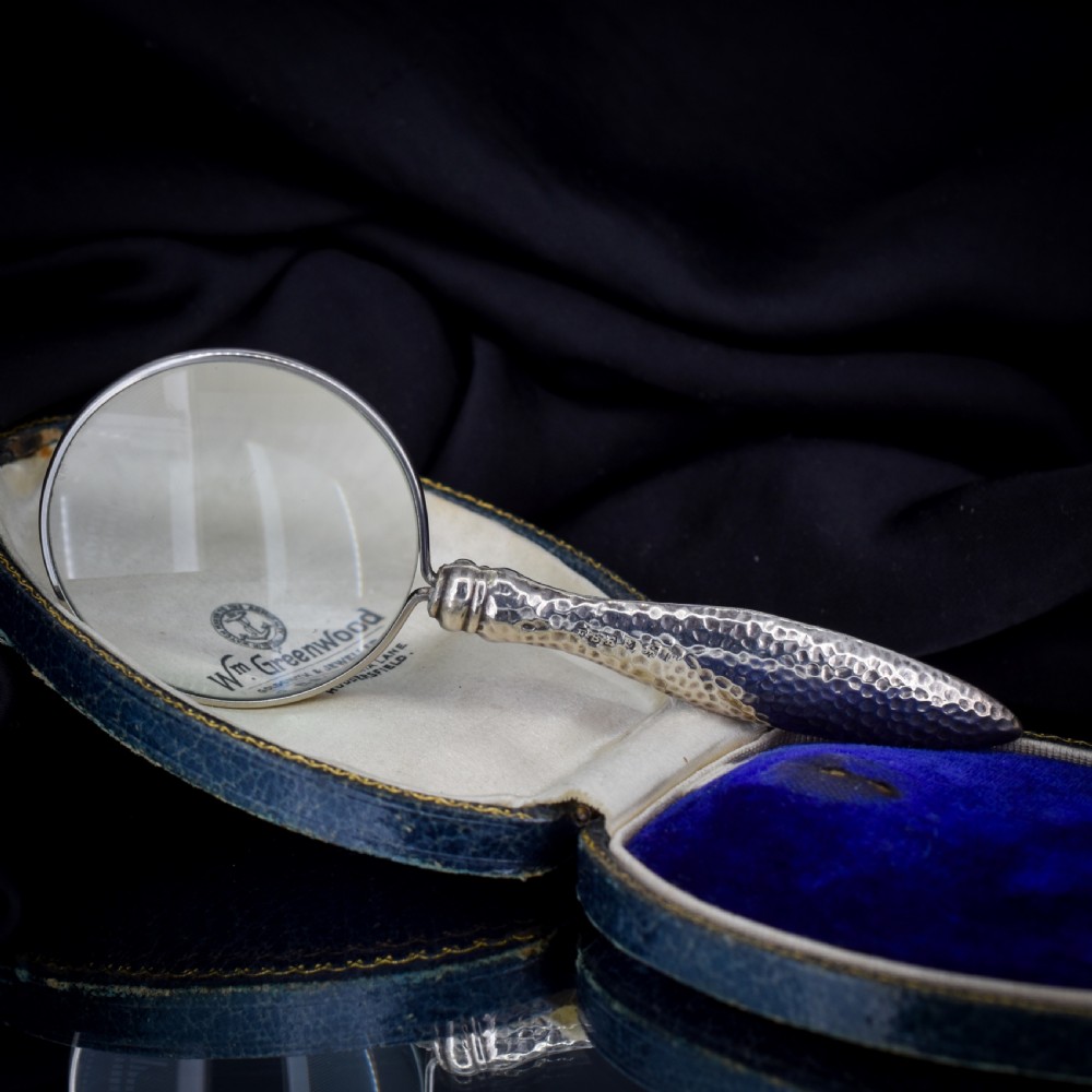 An Edwardian sterling silver magnifying glass featuring a hammered planished handle and a circular glass lens, presented inside an open velvet-lined case. View VIII