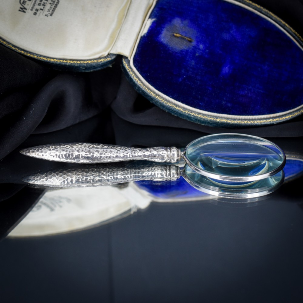 An Edwardian sterling silver magnifying glass featuring a hammered planished handle and a circular glass lens, presented inside an open velvet-lined case. View IX