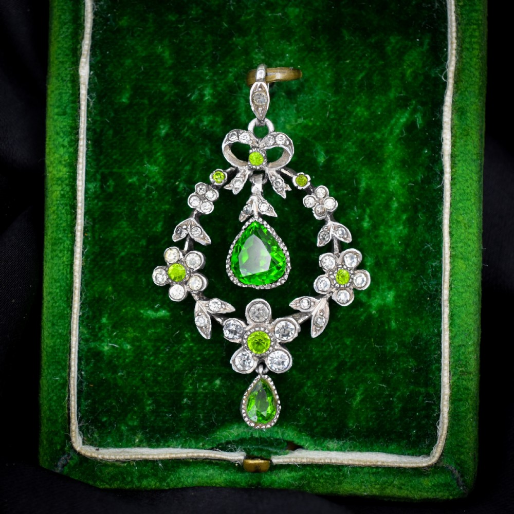 An Edwardian silver openwork floral lavalier pendant set with clear and green paste glass stones featuring a bow motif and suspended green teardrop stone. View II