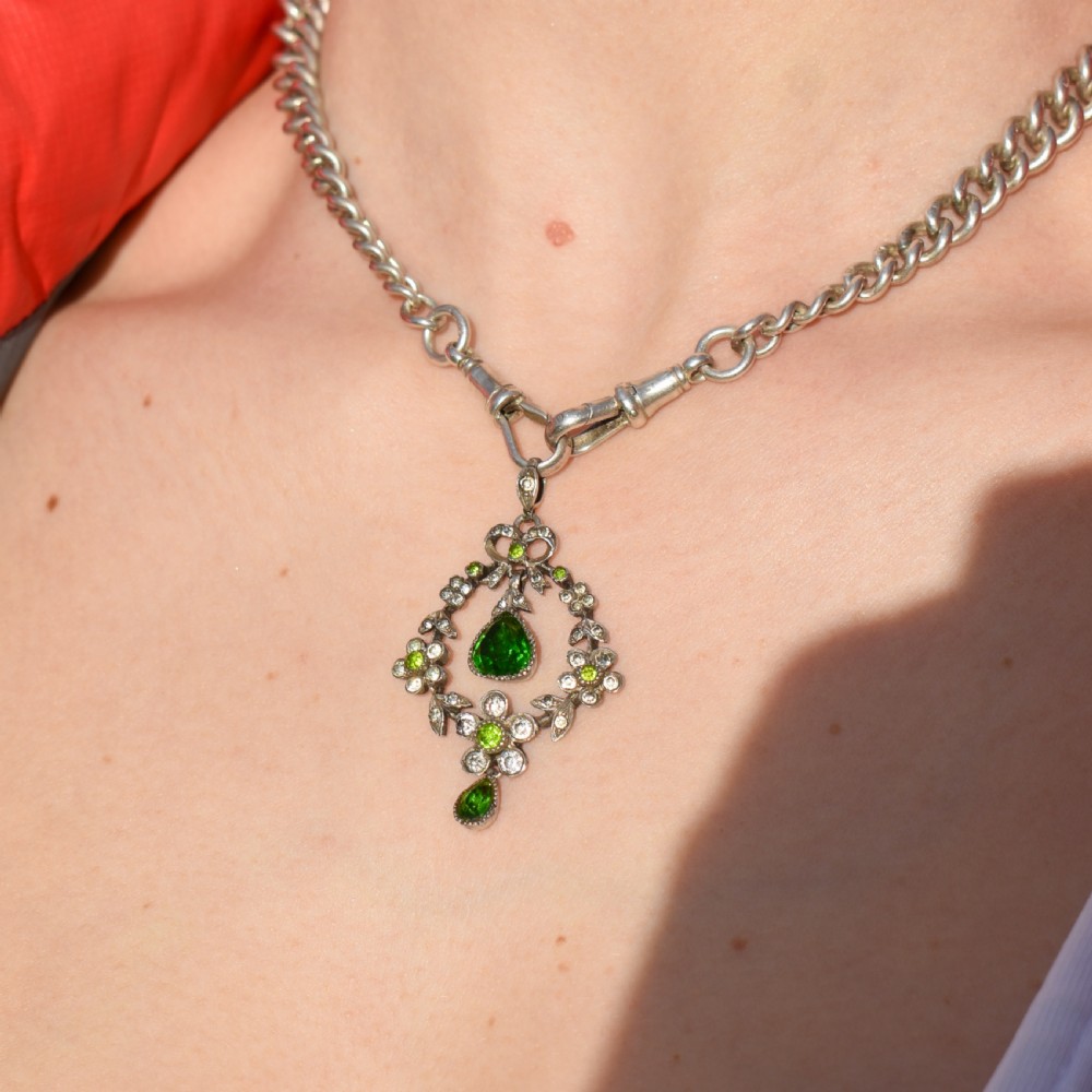 An Edwardian silver openwork floral lavalier pendant set with clear and green paste glass stones featuring a bow motif and suspended green teardrop stone. View III