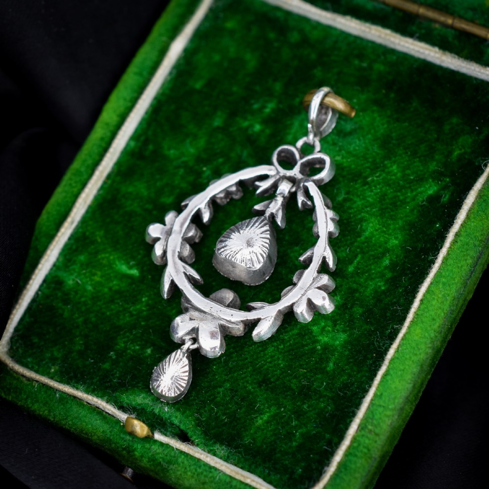 An Edwardian silver openwork floral lavalier pendant set with clear and green paste glass stones featuring a bow motif and suspended green teardrop stone. View VIII