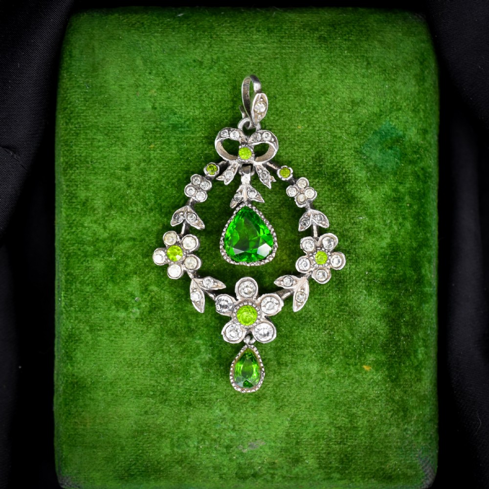 An Edwardian silver openwork floral lavalier pendant set with clear and green paste glass stones featuring a bow motif and suspended green teardrop stone. View IX