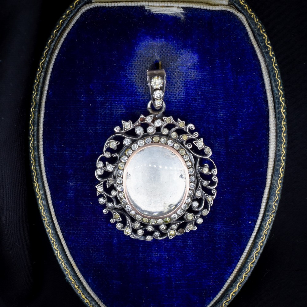 An oval antique locket pendant crafted in silver and gold, featuring an openwork scrollwork border set with old-cut clear paste stones surrounding a central glass compartment.
