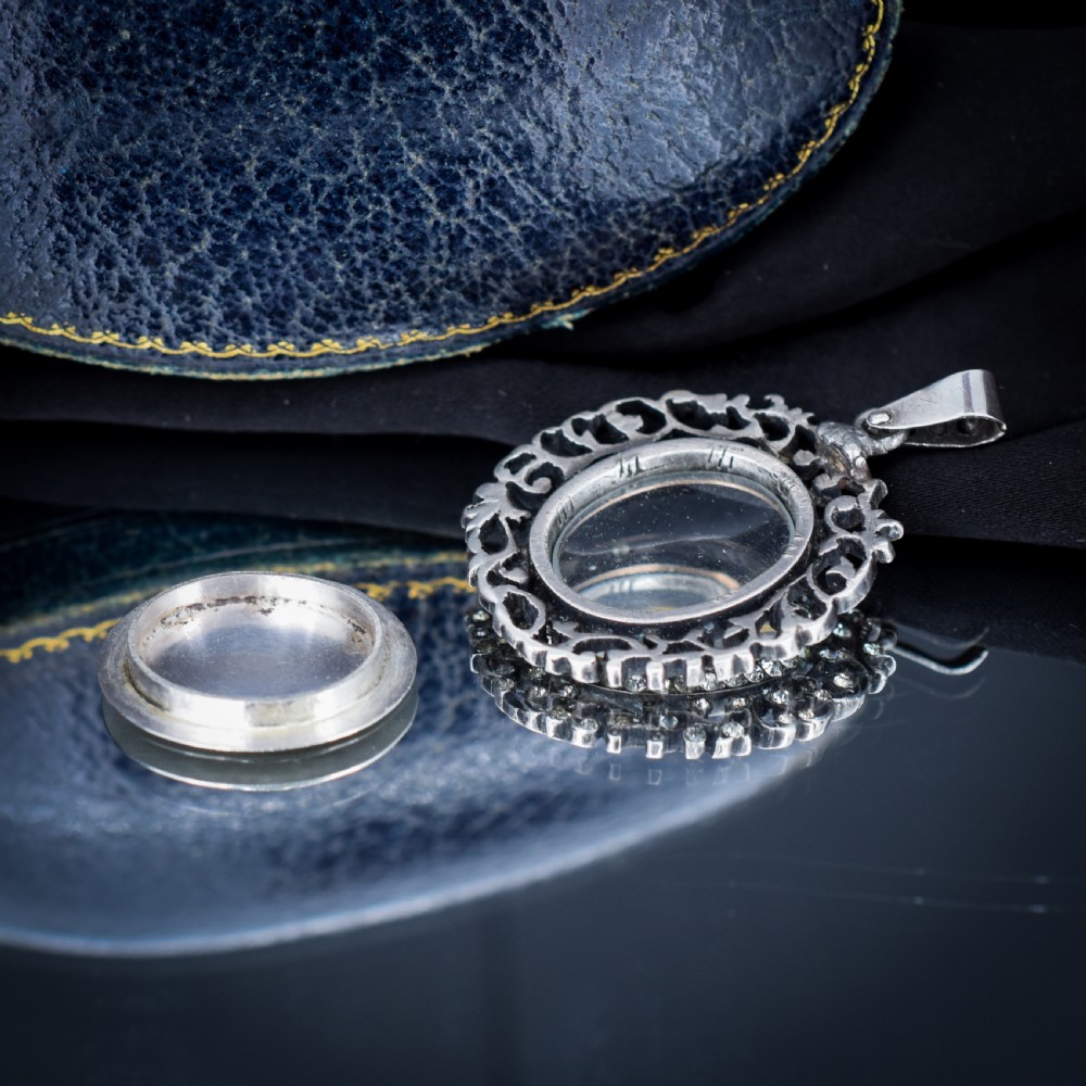 An oval antique locket pendant crafted in silver and gold, featuring an openwork scrollwork border set with old-cut clear paste stones surrounding a central glass compartment. View VII