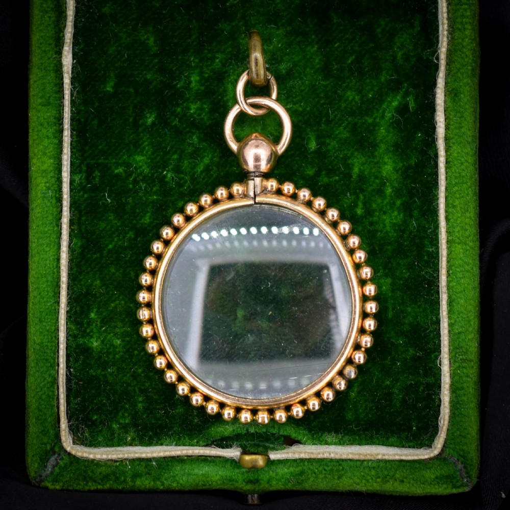 A circular antique gold locket featuring clear glass panels surrounded by a beaded outer border and a top hanging loop.