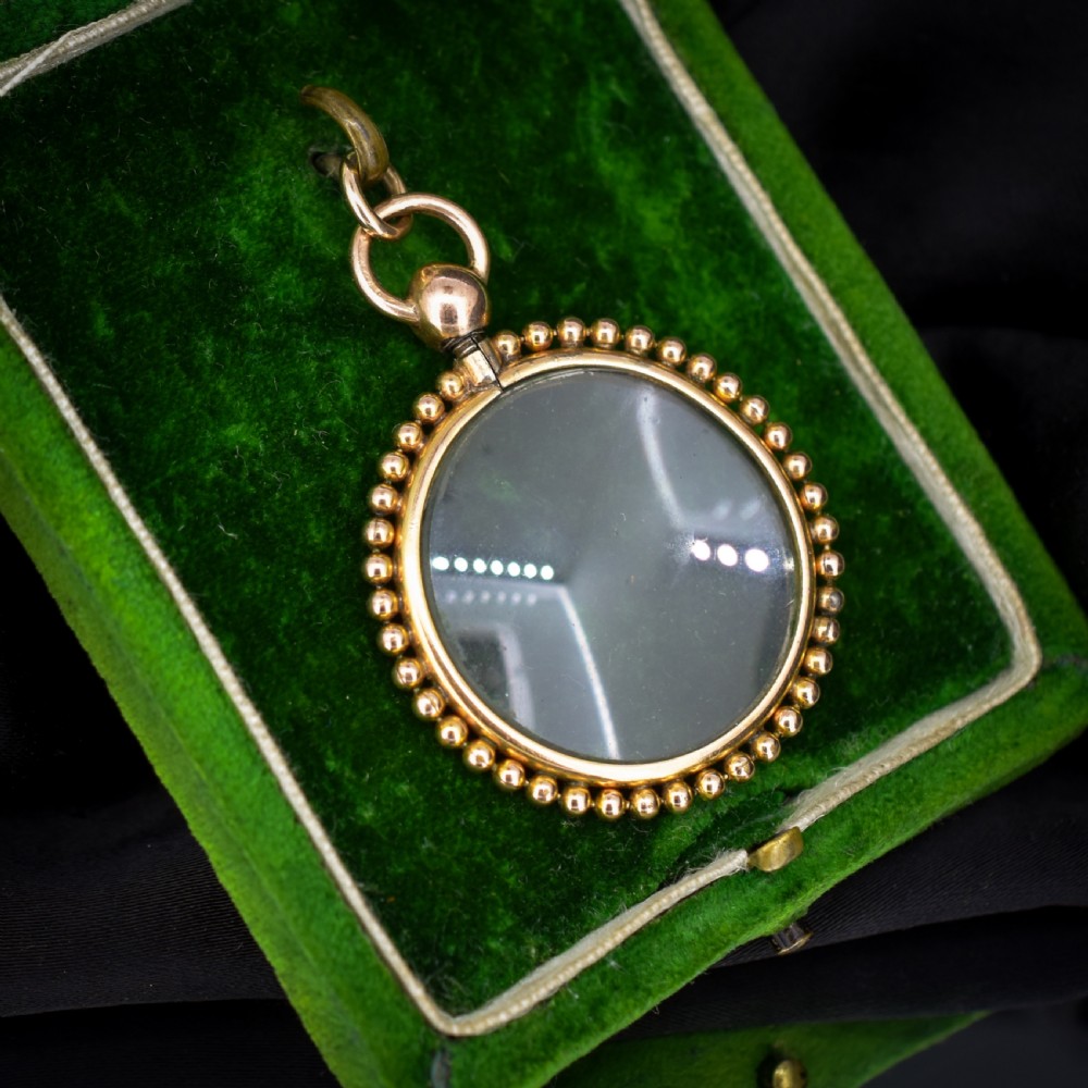 A circular antique gold locket featuring clear glass panels surrounded by a beaded outer border and a top hanging loop. View II