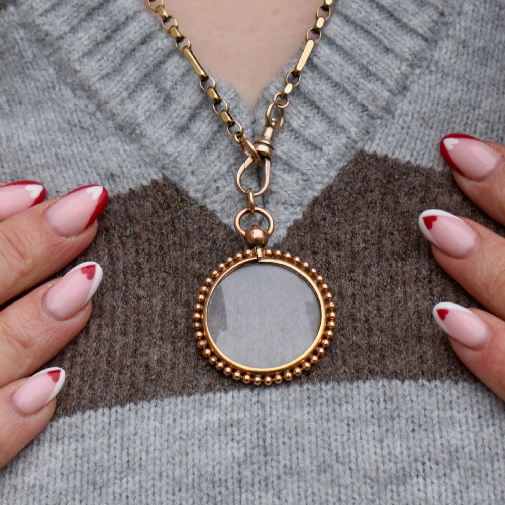 A circular antique gold locket featuring clear glass panels surrounded by a beaded outer border and a top hanging loop. View IV