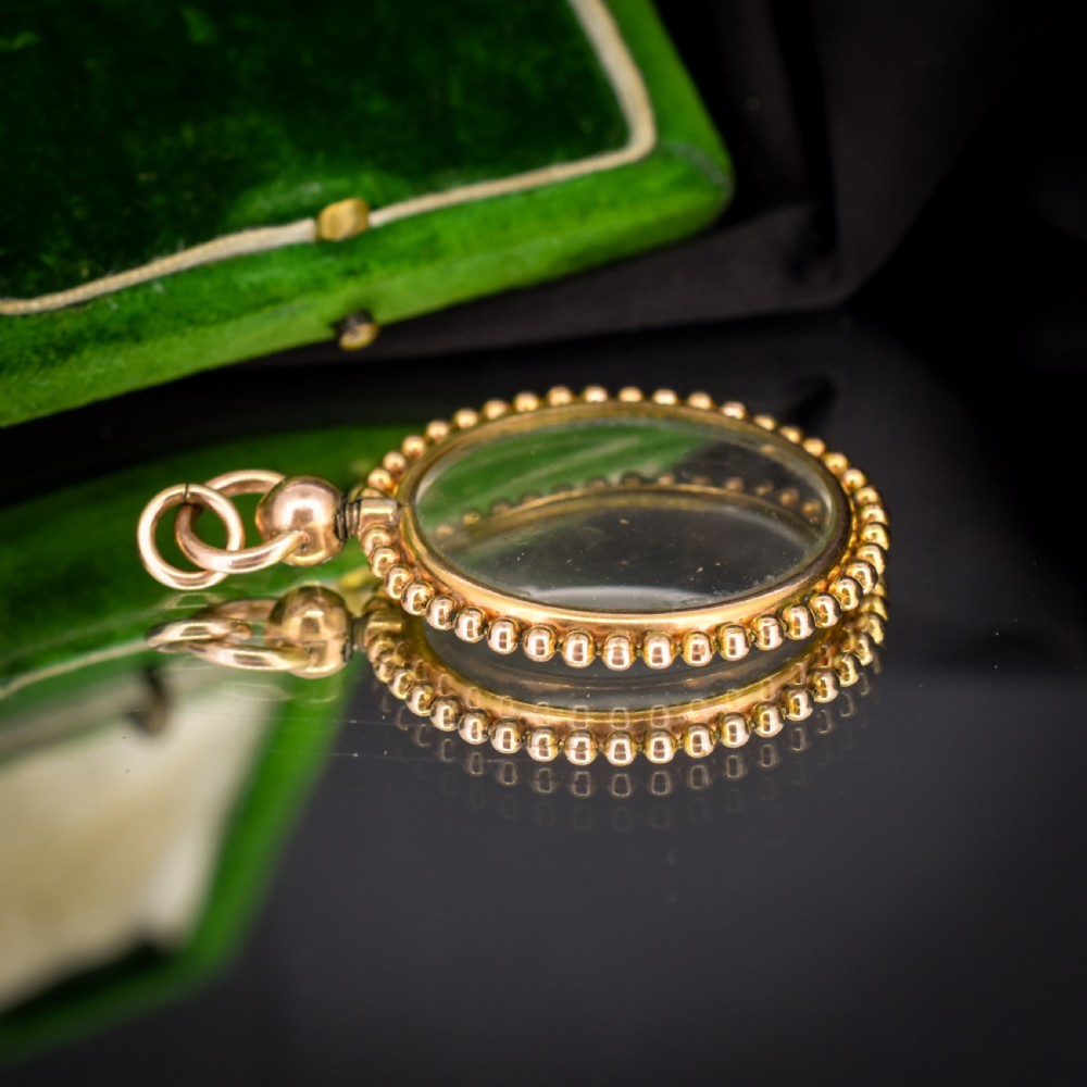 A circular antique gold locket featuring clear glass panels surrounded by a beaded outer border and a top hanging loop. View V