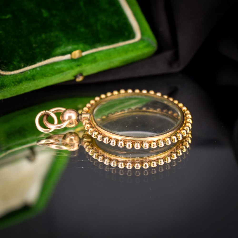 A circular antique gold locket featuring clear glass panels surrounded by a beaded outer border and a top hanging loop. View VII