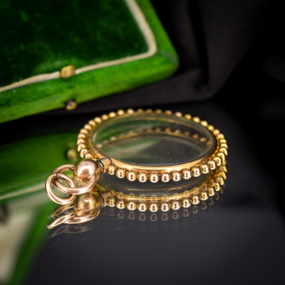 A circular antique gold locket featuring clear glass panels surrounded by a beaded outer border and a top hanging loop. View VIII