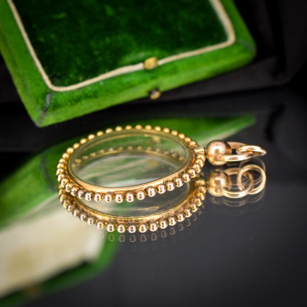 A circular antique gold locket featuring clear glass panels surrounded by a beaded outer border and a top hanging loop. View IX
