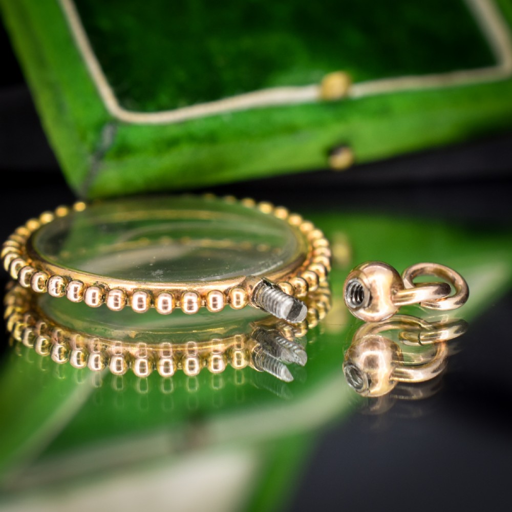 A circular antique gold locket featuring clear glass panels surrounded by a beaded outer border and a top hanging loop. View X