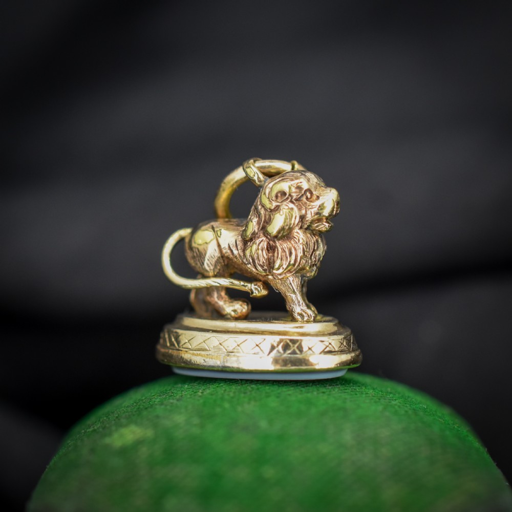 An antique gold fob seal featuring a three-dimensional standing lion figure on an engraved oval base set with a sardonyx stone.
