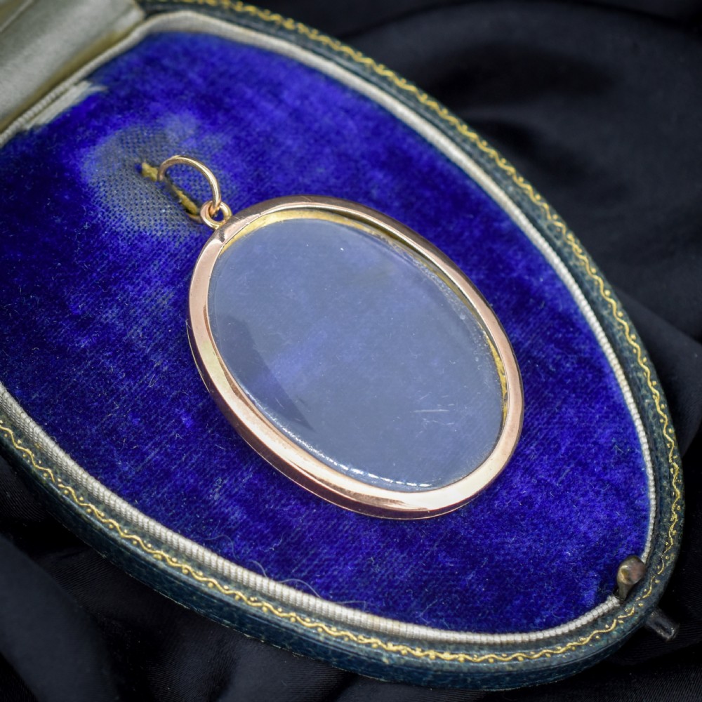 An antique oval 9ct gold photo locket featuring clear double-sided glass panels and a suspension ring set inside a velvet box.