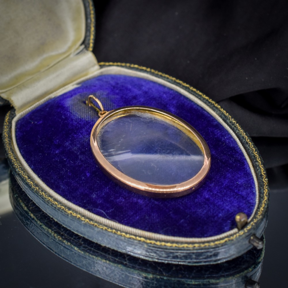 An antique oval 9ct gold photo locket featuring clear double-sided glass panels and a suspension ring set inside a velvet box. View IV