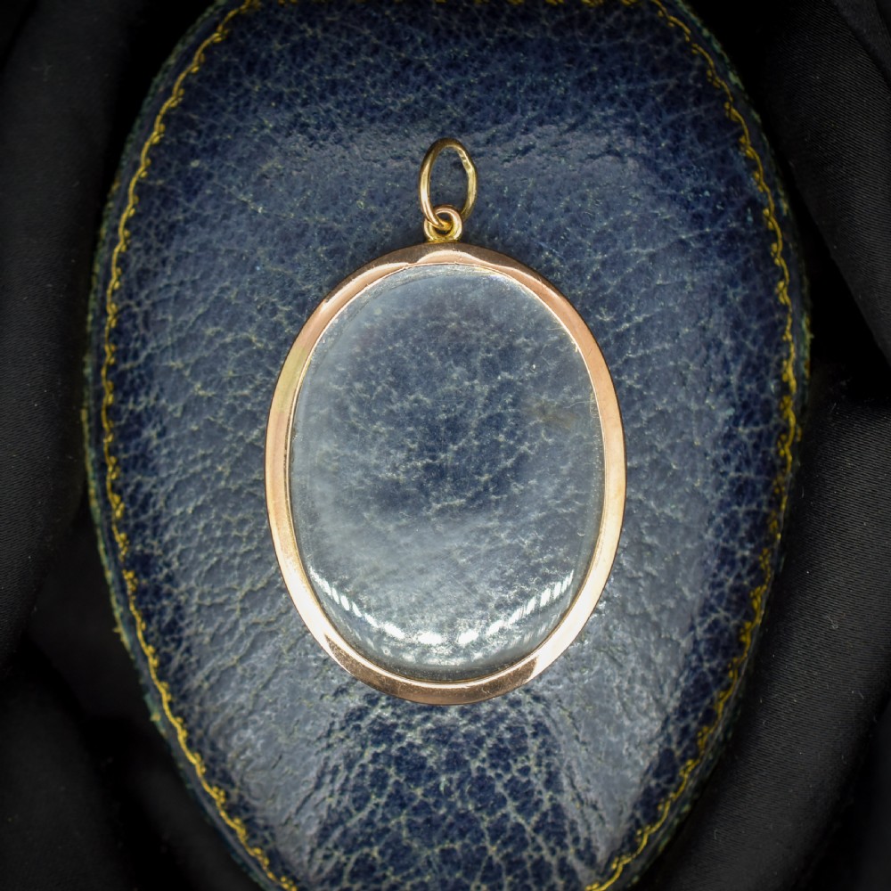 An antique oval 9ct gold photo locket featuring clear double-sided glass panels and a suspension ring set inside a velvet box. View VI