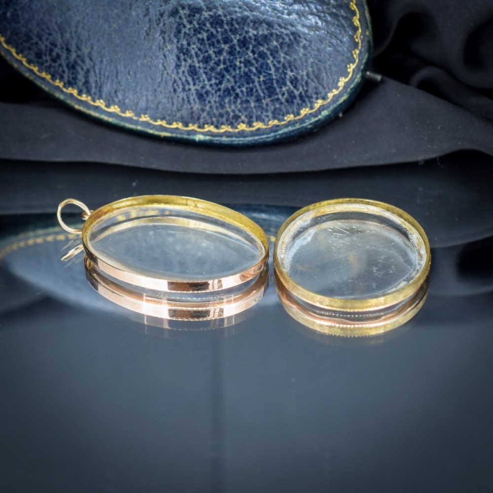 An antique oval 9ct gold photo locket featuring clear double-sided glass panels and a suspension ring set inside a velvet box. View X