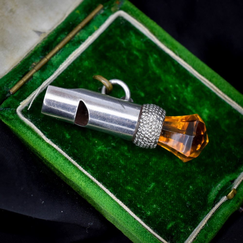 An antique sterling silver whistle pendant shaped like a thistle with a textured body and a faceted amber-coloured glass top.