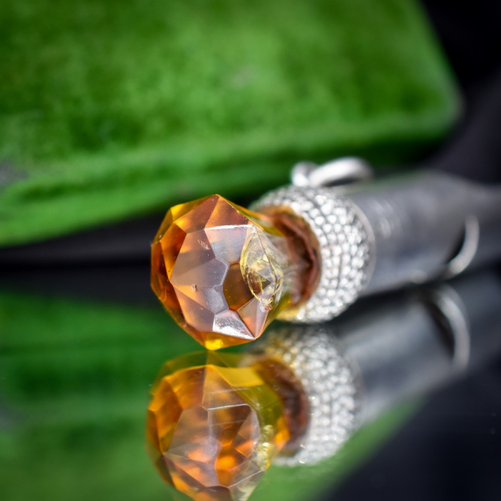 An antique sterling silver whistle pendant shaped like a thistle with a textured body and a faceted amber-coloured glass top. View V
