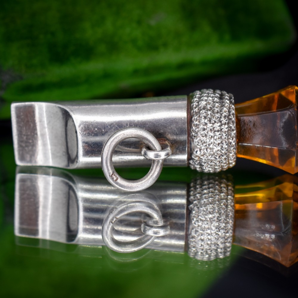 An antique sterling silver whistle pendant shaped like a thistle with a textured body and a faceted amber-coloured glass top. View VII