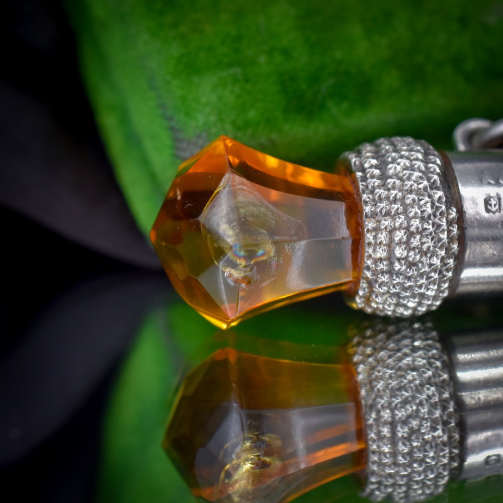 An antique sterling silver whistle pendant shaped like a thistle with a textured body and a faceted amber-coloured glass top. View VIII