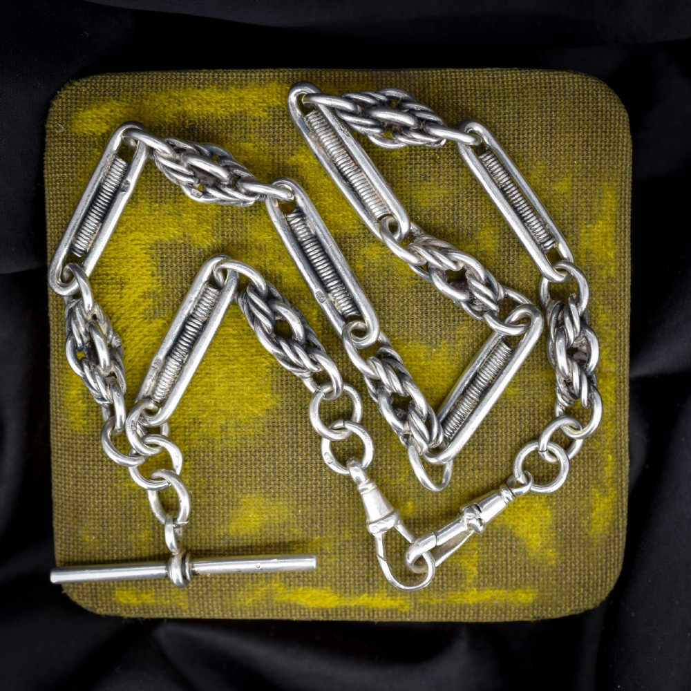 An antique sterling silver Albert chain featuring trombone links, love knot accents, a T-bar fastener, and a swivel dog clip.