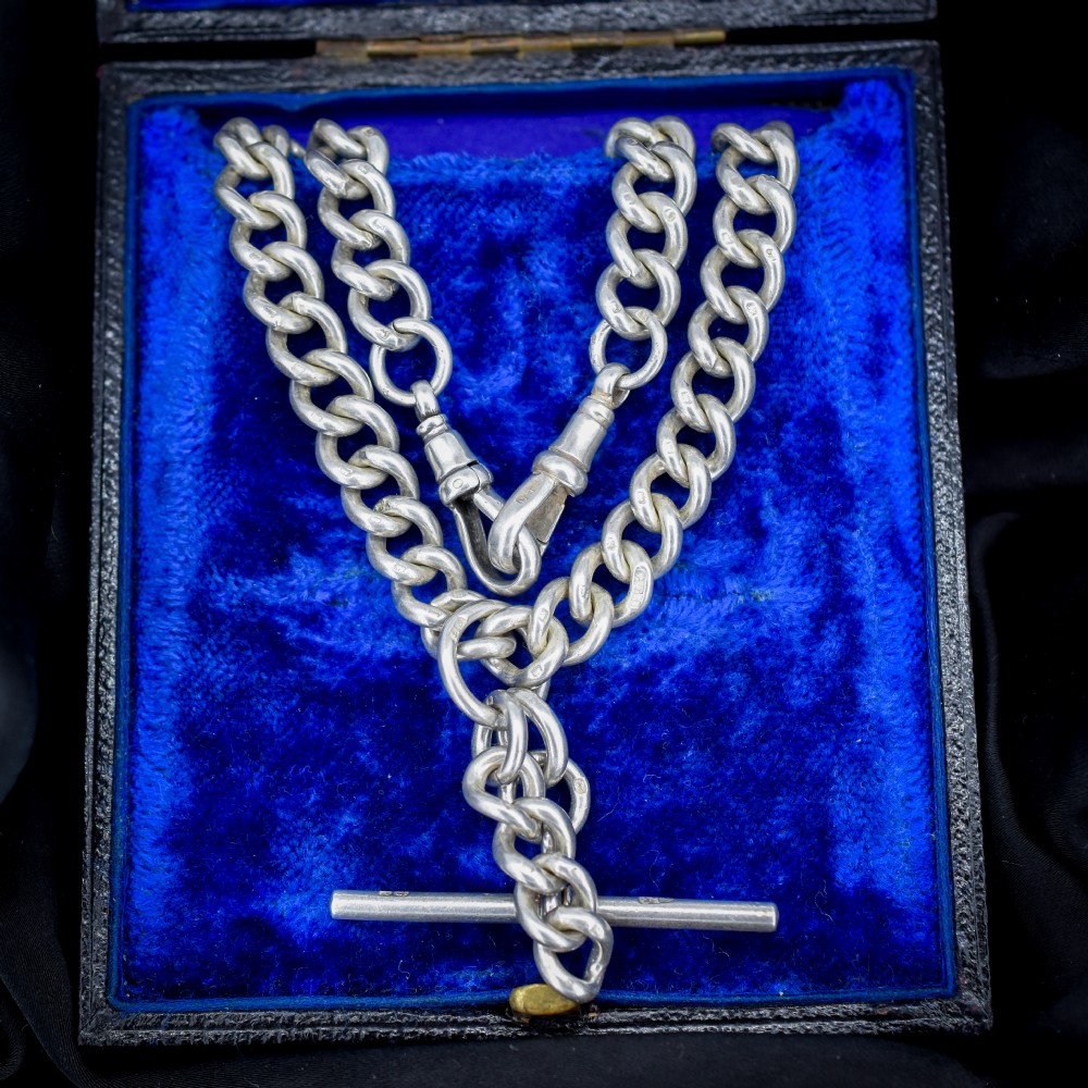 An antique sterling silver curb link Albert watch chain featuring a T-bar and dog clips displayed on blue velvet.