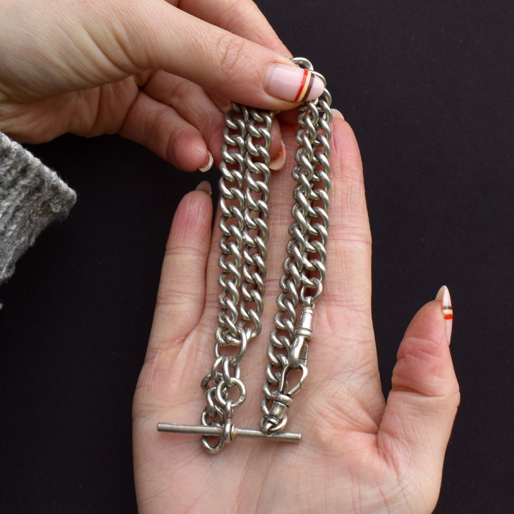 An antique sterling silver curb link Albert watch chain featuring a T-bar and dog clips displayed on blue velvet. View III