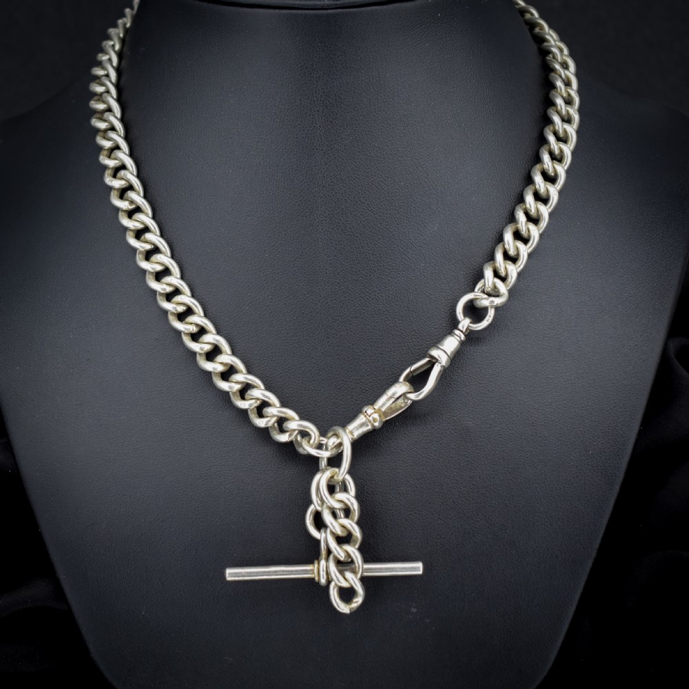 An antique sterling silver curb link Albert watch chain featuring a T-bar and dog clips displayed on blue velvet. View IV