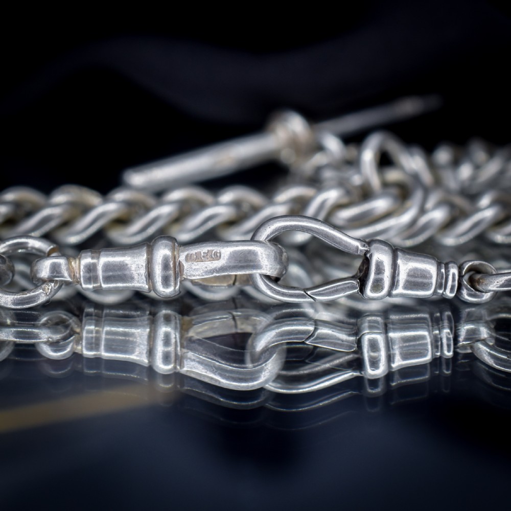 An antique sterling silver curb link Albert watch chain featuring a T-bar and dog clips displayed on blue velvet. View X