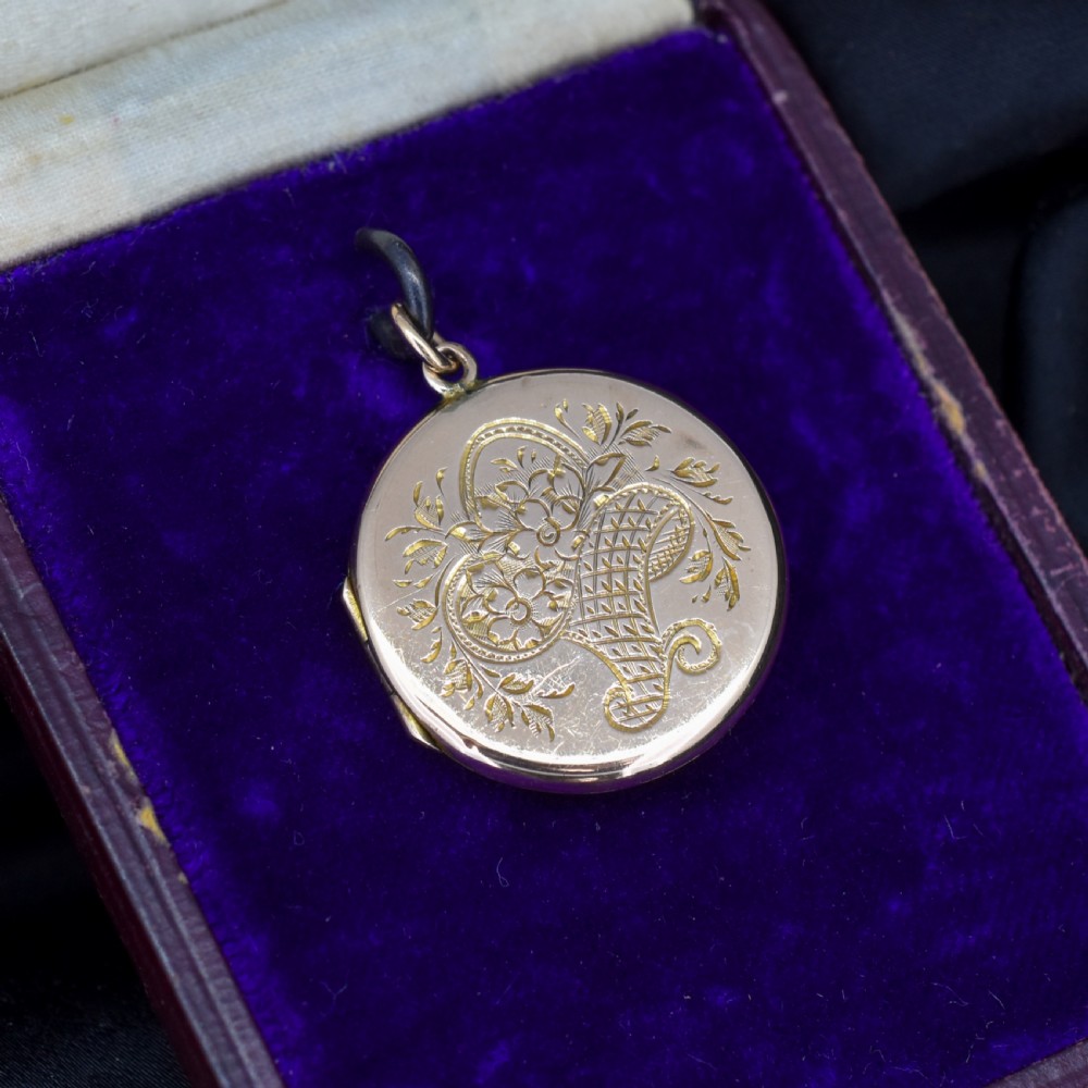 A circular antique yellow gold locket featuring intricate hand engraving of a flower basket motif.