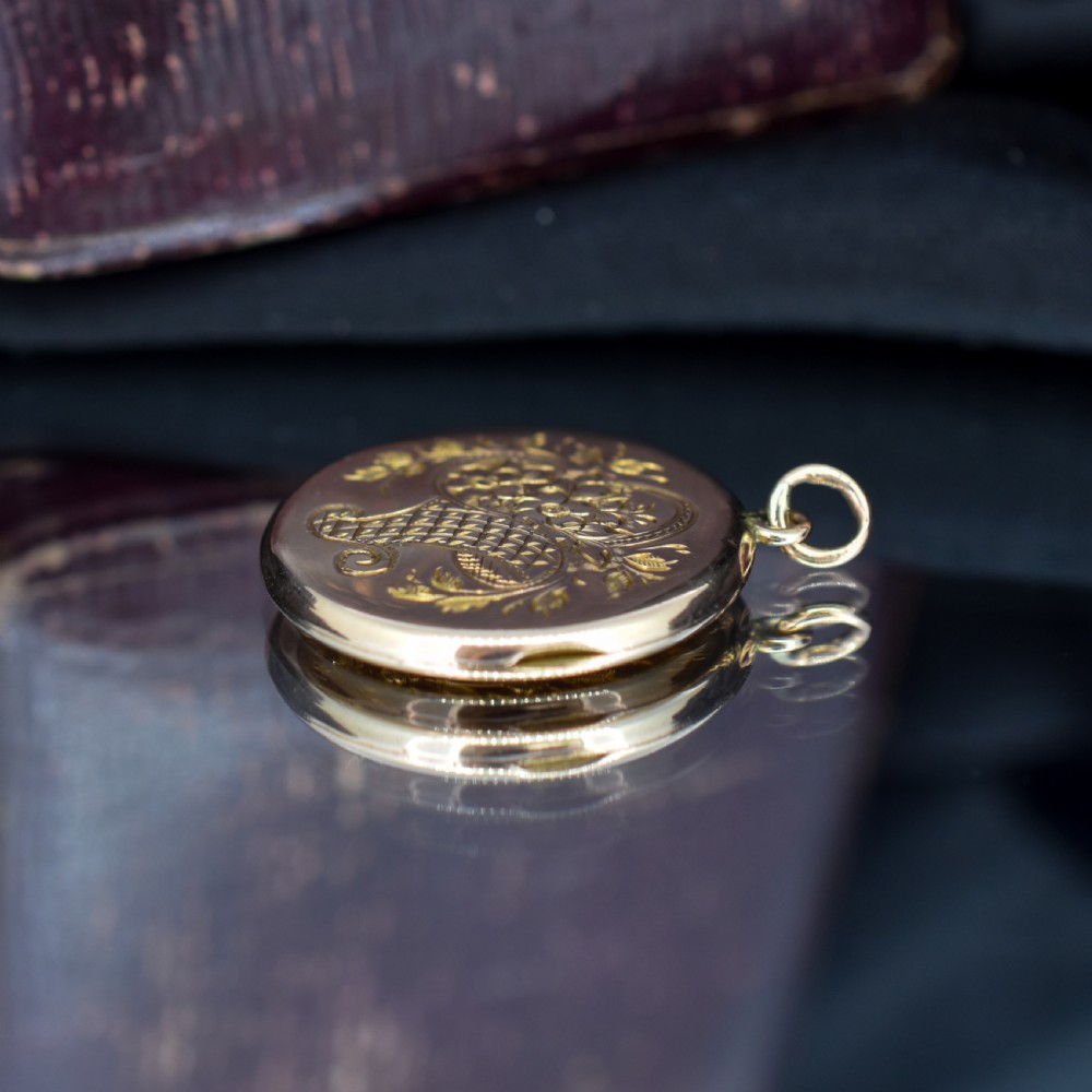 A circular antique yellow gold locket featuring intricate hand engraving of a flower basket motif. View VII